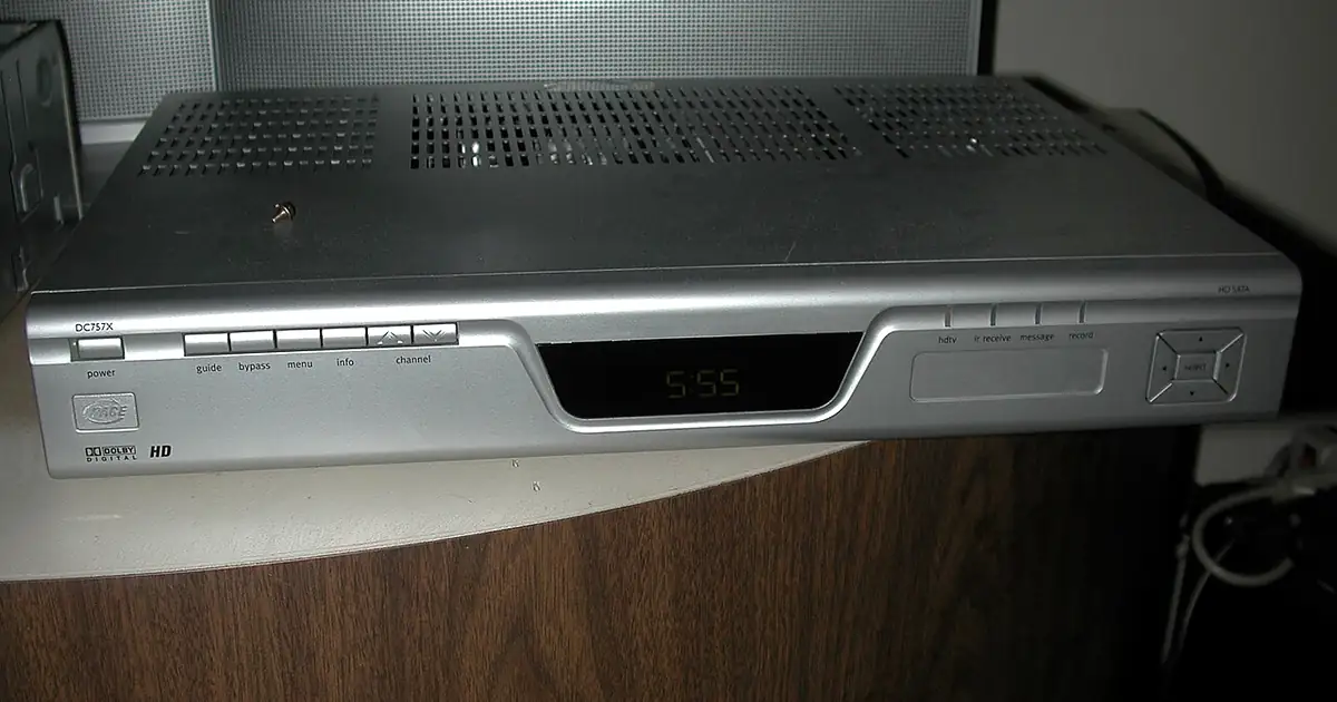 Ancien décodeur câble argenté posé sur un meuble TV, comparé à l’IPTV