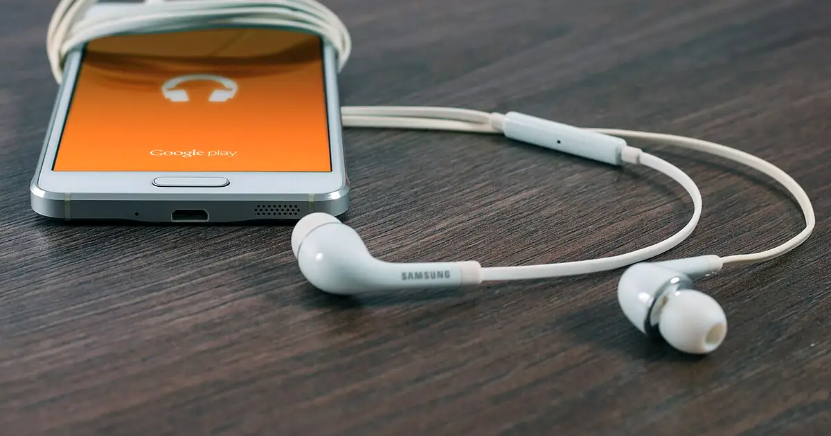 Smartphone Samsung affichant une boutique d’applications, avec des écouteurs posés à côté